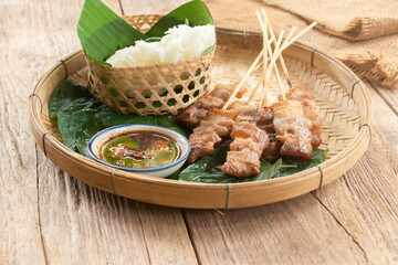 Thai style grilled pork and steamed sticky rice With Jaew dipping sauce on a wooden floor