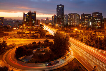 ​Beijing's Sanyuanqiao under twilight: Cityscape with neon-lit highways and streaks of car light...