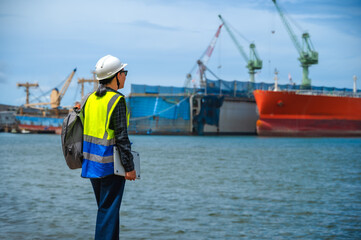Side view female ship engineer holding tablet looking away at ships in the sea