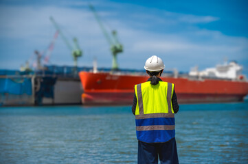 REarview female ship engineer holding tablet looking away at ships in the sea
