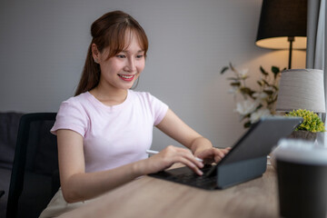 Young asian woman working from home using tablet and keyboard at desk