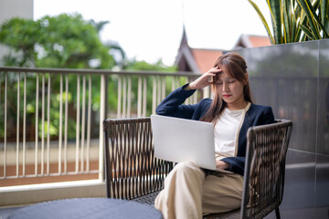 Stressed businesswoman having headache while working on laptop on balcony