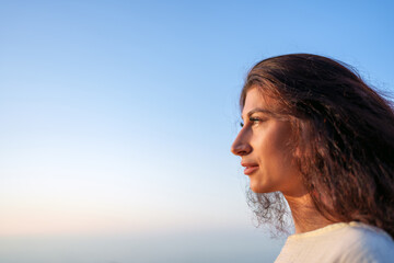 Peaceful woman gazing at vibrant sunset, experiencing tranquil moment with calm facial expression