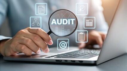 Business professional examines digital audit icons through a magnifying glass over a laptop