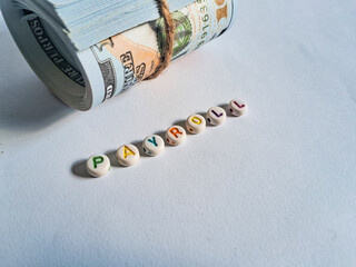 Creative payroll concept with rolled US dollar  and colorful alphabet beads spelling 