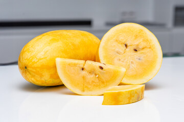 Yellow watermelon slice on reflective white surface with whole fruit in background