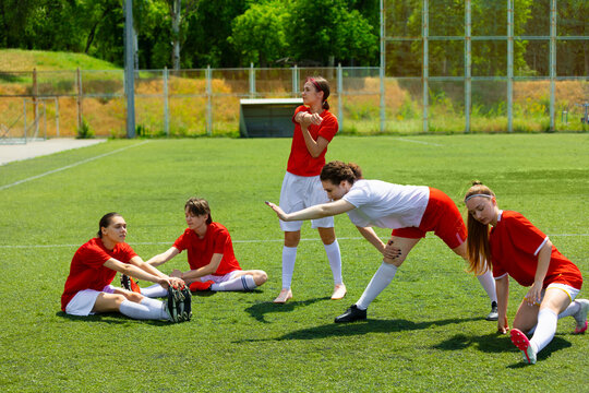 Women soccer team stretching and preparing during practice on sunny sports field. Concept of group motivation, stretching session, sports education and body-positive support atmosphere.