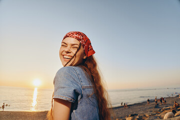 smiling woman in modern boho-western denim jacket enjoys sunset on beach, film color tones, casual...