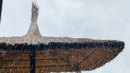 Tropical rain falling behind window with straw sunshade view.