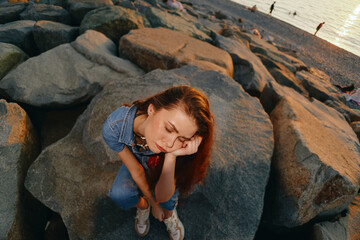 lifestyle woman in modern boho-western denim street style sitting on rocks at sunset, contemplative mood, warm film color grading, casual outfit, serene atmosphere