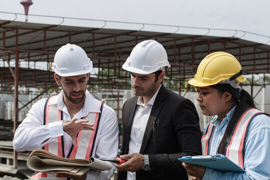 Team of engineers reviewing construction documents and plans on site. Surrounded by concrete panels and heavy machinery, they demonstrate teamwork and coordination in a real industrial setting.