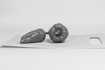 Two green bell peppers lie on a light gray cutting board. The peppers are fresh, one is positioned vertically and the other is lying on its side, highlighting their bright color.