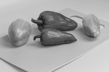 Green and yellow bell peppers are placed on a light gray cutting board. The peppers have a smooth, shiny surface with whole stems. Preparation for cooking, fresh produce on a neutral background.