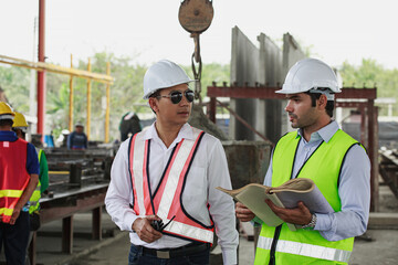 Close-up image of Asian and Caucasian engineers collaborating at a construction site inside precast...