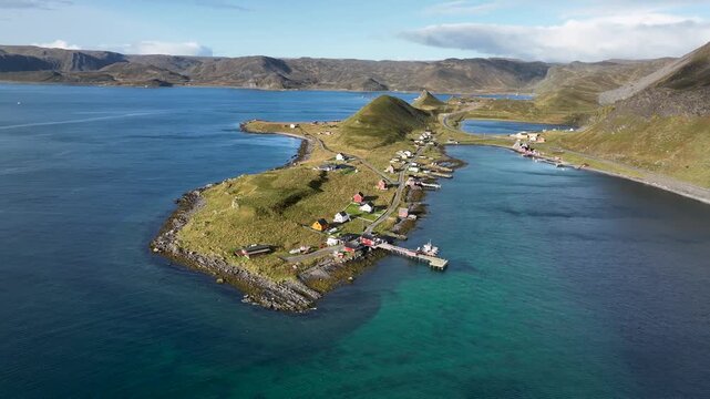 Aerial view of Hamningberg village shows a peninsula with colorful houses, a pier, and the contrast between the turquoise water and the green land, Finnmark, Norway.