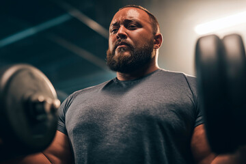 Determined plus-size athlete lifting weights during intense gym workout session