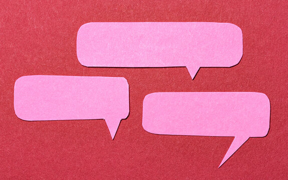 Pink cut out paper speech bubbles with copy space for text on red background, flat lay top view conceptual conversation backdrop