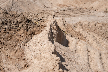 rugged construction landscape featuring dry sandy soil with visible tire tracks and irregular terrain highlighted by warm sunlight creating contrasting shadows, traces, mound, difference, hardpan