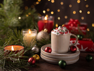 festive holiday scene with creamy hot chocolate in a mug, surrounded by twinkling candles, pine branches, and colorful wrapped gifts against a soft focus glowing light background, tablescape, craft