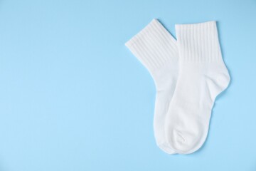 Pair of comfortable white socks on light blue background, top view. Space for text