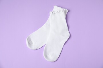 Pair of comfortable white socks on violet background, top view