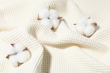 Clean waffle towel and cotton flowers as background, top view