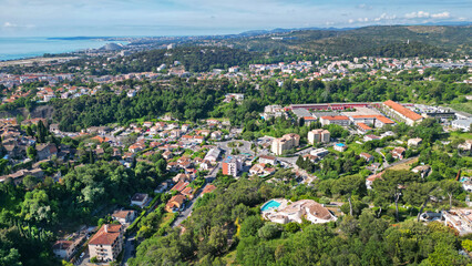 Fototapeta premium Aerial view of a vibrant residential area surrounded by lush greenery and hills, showcasing a mix of modern and traditional architecture with a distant coastline