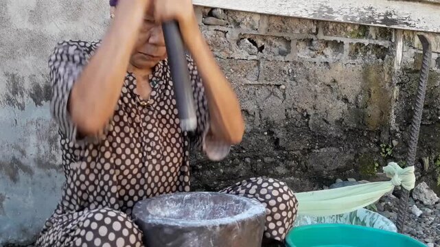 A woman manually pounds rice using a mortar or pestle, a traditional tool for grinding rice into flour. This traditional method is still used in Aceh Province.