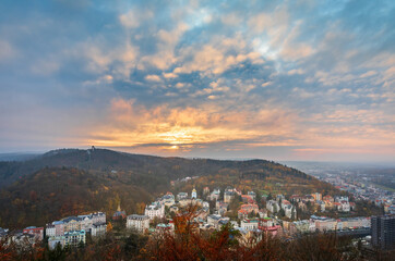 Autumn cityscape of Karlovy Vary, Czech Republic. Historic spa town with colorful buildings, church towers, river promenade, and forested hills in golden fall foliage.
