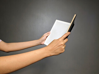 Close-up of a person's hands holding an open notebook with lined pages against a plain dark gray...