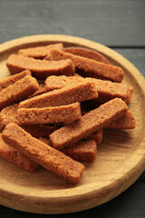 Tasty rye croutons on wooden plate on black background.