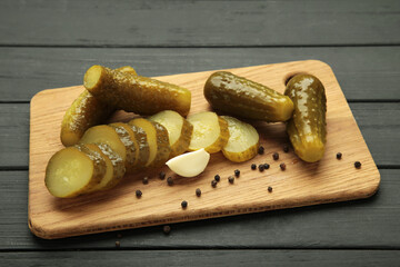 Marinated pickled cucumber on cutting board on black wooden background.