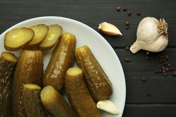 Marinated pickled cucumber with garlic on black wooden background.