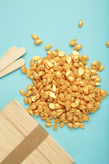 Beautiful gold depilatory wax granules and wooden spatulas on blue background. Epilation,...