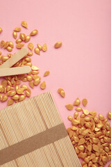 Beautiful gold depilatory wax granules and wooden spatulas on pink background. Epilation,...