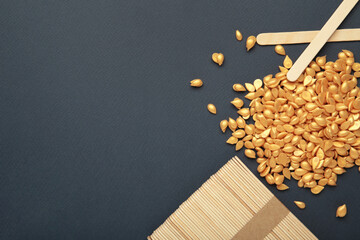 Beautiful gold depilatory wax granules and wooden spatulas on dark blue background. Epilation,...