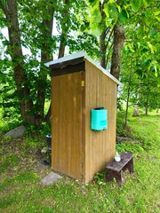 Rustic outdoor wooden toilet with a plastic hand-washing container attached to the side wall.