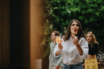 A cheerful woman holds a refreshing drink while socializing outdoors, exuding joy and relaxation....