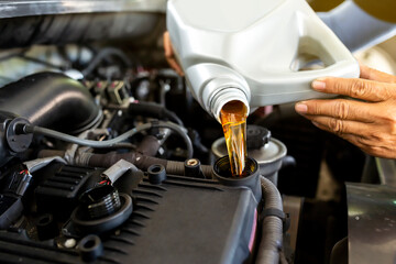 Car mechanic replacing and pouring fresh oil into engine at maintenance repair service station.
