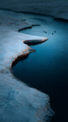 Glacial river surrounded by ice formations and birds in flight during a serene twilight setting
