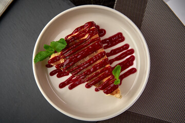A Delicious Slice of Cake Topped with Rich Berry Sauce and Fresh Mint Leaves Perfectly Arranged on a White Plate for an Irresistible Dessert Experience