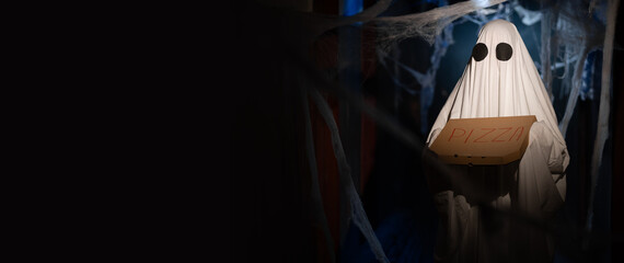 Funny halloween ghost in white sheet holding box with favorite pizza in dark room with cobweb....