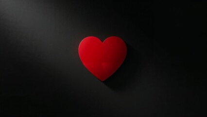A single red heart, a symbol of love and romance, is dramatically lit and isolated on a dark minimalist background.