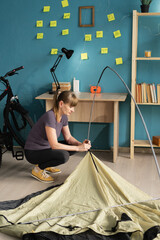 Woman assembling camping tent at home preparing for hike. Trip preparation