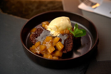 Indulgent Chocolate Cake Topped with Sweet Fruit Compote and Creamy Vanilla Ice Cream Served on a Sleek Black Plate Enhancing the Dessert Presentation