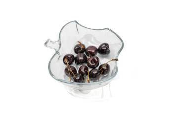 Cherries in Glass Bowl White Background. A transparent glass bowl in a decorative shape is filled with dark cherries. The cherries are shiny and fresh, the background is white.