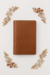 A brown leather journal rests on a white surface, surrounded by dried floral elements.