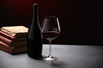 Red wine and stacked books on grey textured table against black background, closeup