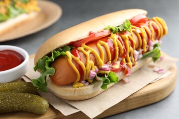 Delicious hot dog with sauces, lettuce, onion and pickles on grey textured table, closeup