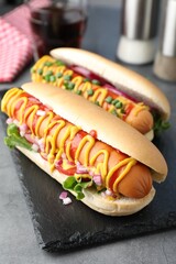 Delicious hot dogs with sauces, lettuce and onion on grey textured table, closeup